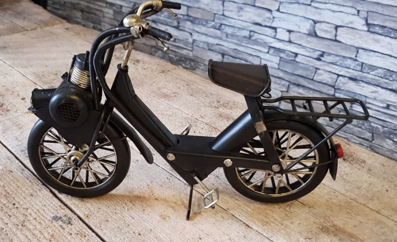 Vintage Solex Bromfiets – Zwart Blik – Decoratief Retro Model 1 Solex Bromfiets vintage zwart prachtig decoratief model voor iedereen die houdt van retro voertuigen en klassieke details. Het model is gemaakt van stevig zwart blik en heeft een authentieke uitstraling. Door de subtiele verouderde look past het perfect in een industrieel, landelijk of nostalgisch interieur. De Solex is compact van formaat en daardoor makkelijk neer te zetten op een wandrek, dressoir, bureau of in een vitrinekast. Het is een leuk item voor verzamelaars, maar ook een origineel cadeau voor iemand die dol is op oude bromfietsen of unieke woonaccessoires. De details van het model zijn zorgvuldig uitgewerkt. Denk aan het herkenbare frame, de klassieke wielen en de typische Solex‑vorm. Hierdoor voelt het alsof je een klein stukje geschiedenis in huis haalt. Het model is decoratief en niet bedoeld om mee te spelen, maar juist om te bewonderen. Gebruik dit retro bromfietsje als eyecatcher in je woonkamer, mancave, werkplek of winkelpresentatie. Het brengt sfeer, karakter en een vleugje nostalgie in elke ruimte. Kenmerken: Materiaal: blik Kleur: zwart Stijl: retro / vintage Decoratief schaalmodel